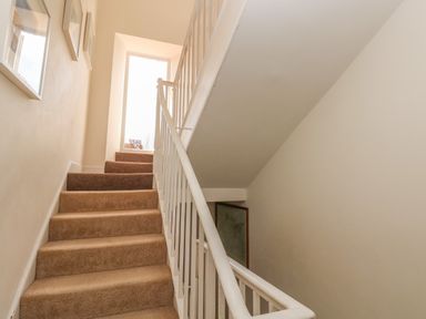 A carpeted staircase with white railings and framed pictures on the wall at Berlin House in Tenby