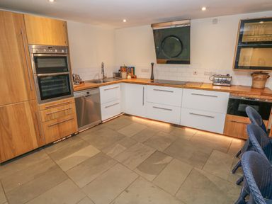 A kitchen with wooden and white cabinets a double oven a dishwasher a sink a toaster and blue chairs at Berlin House in Tenby