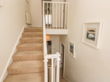 A carpeted staircase with framed pictures on the wall and a white safety gate at Berlin House in Tenby