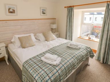A bedroom with a double bed two bedside tables a window with curtains and folded towels on the bed at Berlin House in Tenby