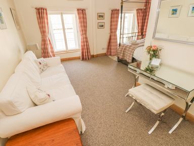 A bedroom with a white sofa, checkered curtains, a metal bed frame, and a mirrored dressing table with a stool at Berlin House in Tenby