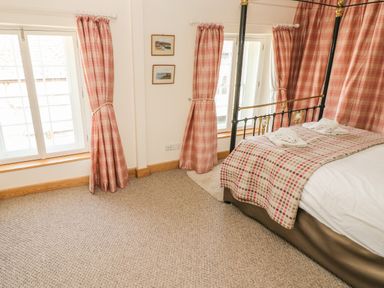 A bedroom with a four-poster bed, pink curtains, two framed pictures on the wall, and a window at Berlin House in Tenby