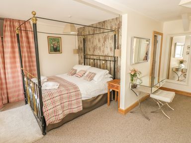 A bedroom with a four-poster bed a bedside table a mirrored dressing table and a stool at Berlin House in Tenby