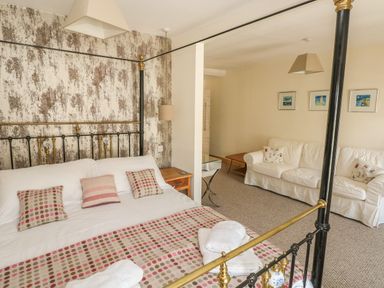 A bedroom with a four-poster bed and a sitting area with white sofas at Berlin House in Tenby