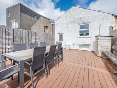 An outdoor patio with a long table and chairs next to a white building at Berlin House in Tenby