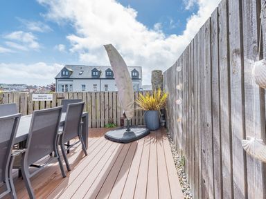 An outdoor deck area with a table and chairs a covered umbrella a plant and wooden fencing at Berlin House in Tenby