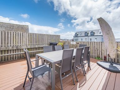 An outdoor wooden deck with a rectangular table and eight chairs surrounded by a wooden fence and a covered umbrella at Berlin House in Tenby