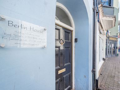 The entrance door of Berlin House holiday accommodation on a street with neighboring shops in Tenby