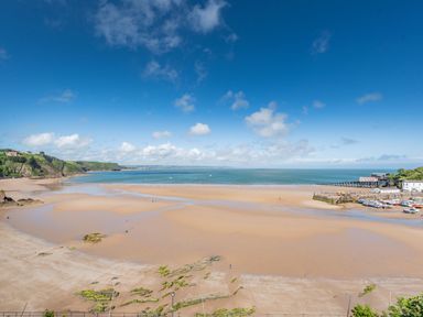 A beach with sand and rocks by the sea with a pier and boats docked at Berlin House in Tenby