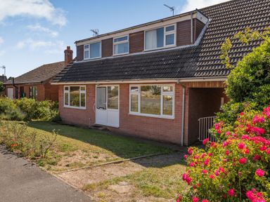 A house with a tiled roof and white framed windows and door with flowering bushes in a front garden at 38 Dale End in Brancaster Staithe near Burnham Market