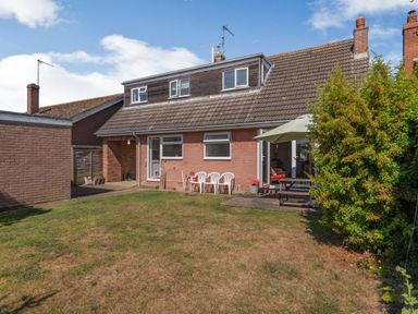 A backyard with a grass lawn plastic chairs a wooden table with an umbrella and a brick house at 38 Dale End in Brancaster Staithe near Burnham Market