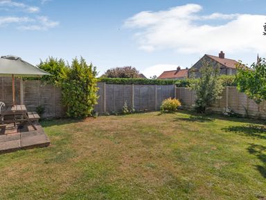 A fenced backyard with grass shrubs and a picnic table with parasol at 38 Dale End in Brancaster Staithe near Burnham Market