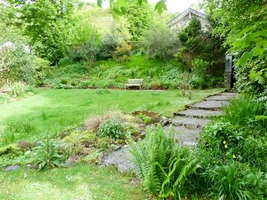 A garden with grass lawn stone pathway bench and dense greenery at The Old Laundry in Clappersgate near Ambleside