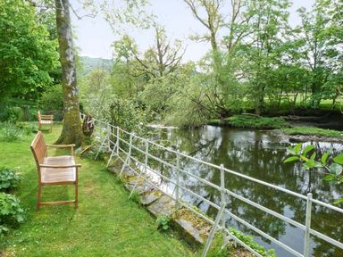 A garden with wooden benches and a metal fence beside a river at The Old Laundry in Clappersgate near Ambleside