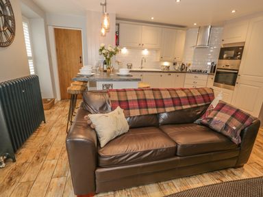 A kitchen with a brown leather sofa and kitchen island with stools at The Old Laundry in Clappersgate near Ambleside