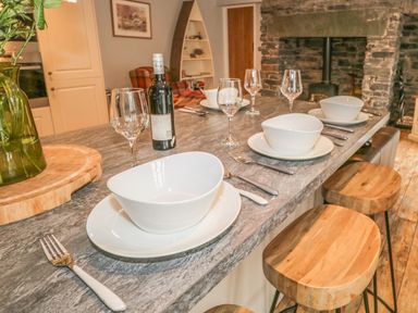 A kitchen island with dining setup and wooden stools near a stone fireplace at The Old Laundry in Clappersgate near Ambleside