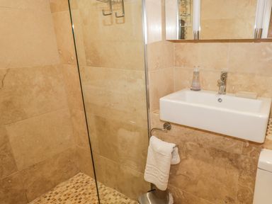 A bathroom with a sink towel holder trash bin and a glass shower partition at The Old Laundry Clappersgate near Ambleside