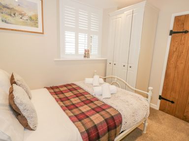 A bedroom with a bed covered by a blanket and pillows towels on the bed a white wardrobe a wooden door and a window with shutters at The Old Laundry Clappersgate near Ambleside