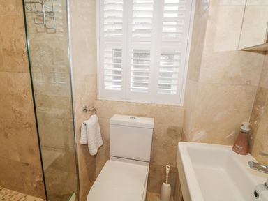 A bathroom with a toilet sink shower and window with shutters at The Old Laundry in Clappersgate near Ambleside
