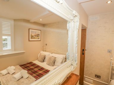 A bedroom with a bed reflected in a large ornate mirror at The Old Laundry in Clappersgate near Ambleside