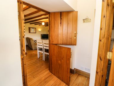 A wooden floor hallway with built in wooden cupboards and a view into a dining and living area at The Barn Cottage in Steel near Hexham