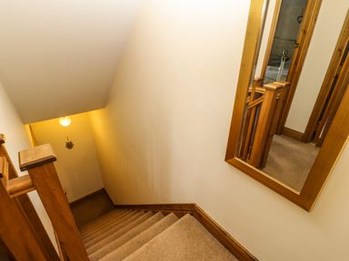 A carpeted staircase with wooden banisters and a wall mirror showing a hallway at The Barn Cottage in Steel near Hexham