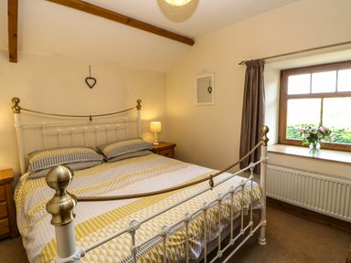 A bedroom with a metal bed frame a window with flowers on the sill and bedside tables with lamps at The Barn Cottage Steel near Hexham