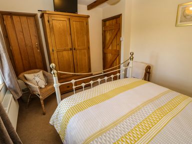 A bedroom with a bed a wooden wardrobe a wicker chair and two wooden doors at The Barn Cottage Steel near Hexham