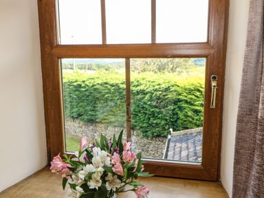 A wooden framed window with flowers on the windowsill and greenery outside at The Barn Cottage in Steel near Hexham