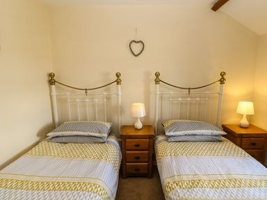 A bedroom with two single beds with patterned bedding and wooden nightstands with lamps between them at The Barn Cottage in Steel near Hexham