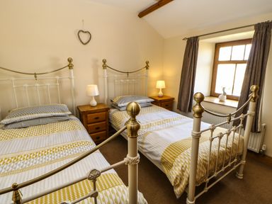 A bedroom with two single beds with patterned bedding two bedside tables with lamps a window with curtains and a heart decoration on the wall at The Barn Cottage Steel near Hexham