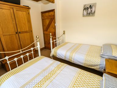 A bedroom with two single beds wooden wardrobe wooden door and a small nightstand at The Barn Cottage in Steel near Hexham