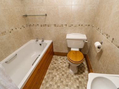 A bathroom with a bathtub wooden panel toilet with wooden seat and tiled walls at The Barn Cottage Steel near Hexham