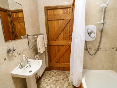 A bathroom with a sink towel rack wooden door shower and bathtub at The Barn Cottage Steel near Hexham