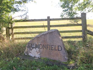 A large rock with the word Salmonfield engraved in front of a wooden fence in a grassy area at The Barn Cottage in Steel near Hexham