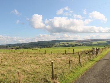 A rural landscape with fenced grassy fields hills and a road at The Barn Cottage in Steel near Hexham