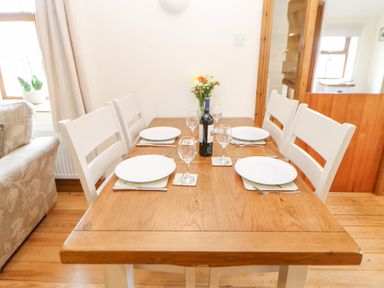 A wooden dining table with four white chairs set with plates glasses cutlery and a bottle of wine at The Barn Cottage Steel near Hexham