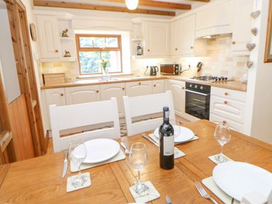 A kitchen with white cabinets a wooden dining table set with plates glasses and a bottle of wine at The Barn Cottage in Steel near Hexham