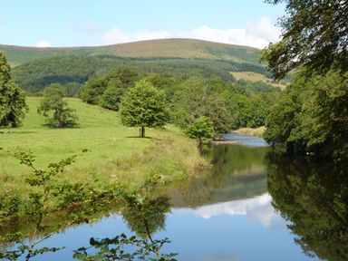 A river flowing beside green fields and trees with hills in the background at The Potting Shed in Burton-in-Kendal near Kirkby Lonsdale
