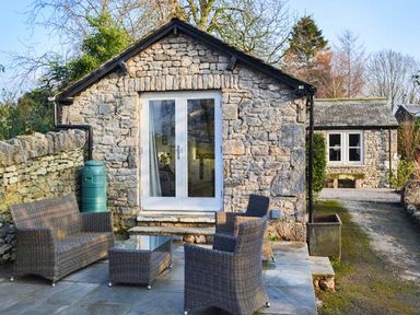 A stone cottage with glass doors and outdoor wicker furniture on a stone patio at The Potting Shed in Burton-in-Kendal near Kirkby Lonsdale