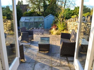 A garden patio with wicker chairs and a glass table in front of a greenhouse and shed at The Potting Shed in Burton-in-Kendal near Kirkby Lonsdale