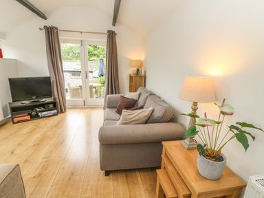 A living room with a sofa, wooden tables, a lamp, a television, and glass doors leading outside at The Potting Shed in Burton-in-Kendal near Kirkby Lonsdale