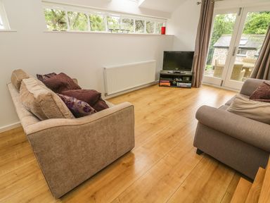 A living room with two sofas a television on a stand and glass doors leading outside at The Potting Shed Burton-in-Kendal near Kirkby Lonsdale