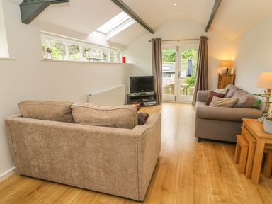 A living room with two sofas a TV on a stand wooden flooring and glass doors at The Potting Shed Burton-in-Kendal near Kirkby Lonsdale