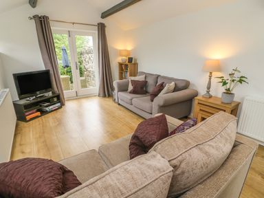 A living room with two sofas a television set on a stand and a side table with a lamp and plant at The Potting Shed Burton-in-Kendal near Kirkby Lonsdale