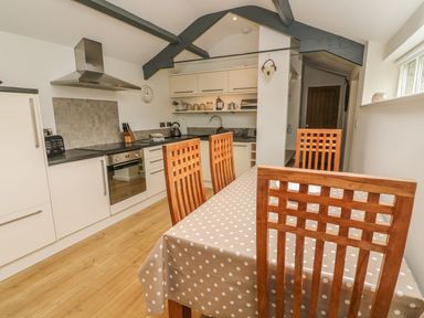 A kitchen with white cabinets wooden chairs and a table with a polka dot tablecloth at The Potting Shed Burton-in-Kendal near Kirkby Lonsdale