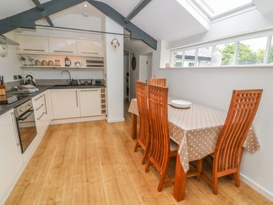 A kitchen with white cabinets a wooden dining table with six chairs and a polka dot tablecloth at The Potting Shed Burton-in-Kendal near Kirkby Lonsdale