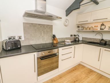 A kitchen with white cabinets black countertop and wooden floor at The Potting Shed in Burton-in-Kendal near Kirkby Lonsdale