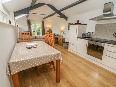 A kitchen and dining area with a tablecloth covered table and wooden chairs next to kitchen cabinets and oven at The Potting Shed in Burton-in-Kendal near Kirkby Lonsdale