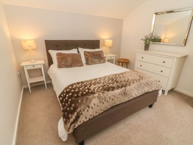 A bedroom with a bed flanked by two bedside tables with lamps and a dresser with a mirror and plant at The Potting Shed Burton-in-Kendal near Kirkby Lonsdale